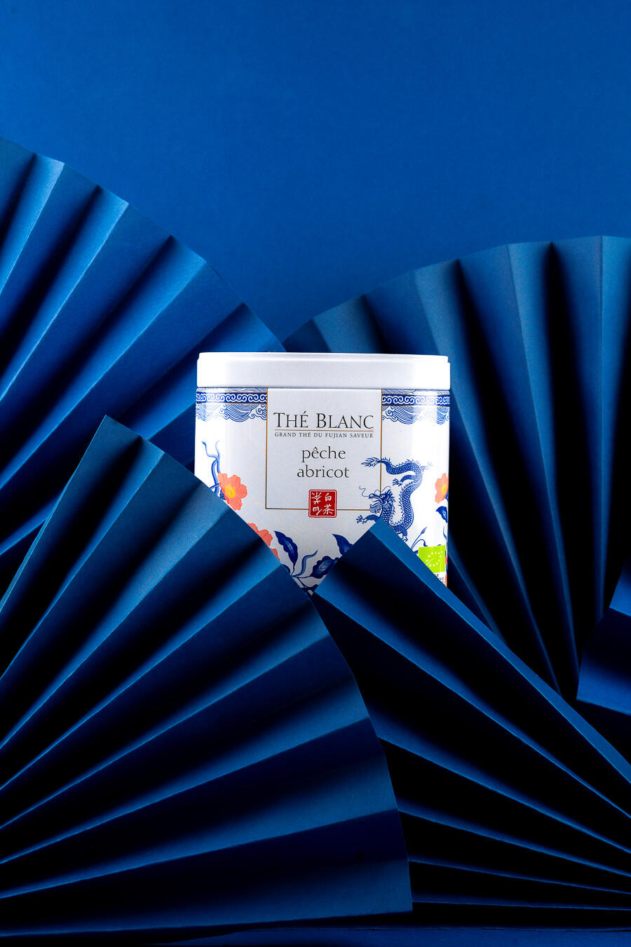 photo ambiance produit culinaire photo d'une boite de thé peche abricot entourée d'éventails bleus