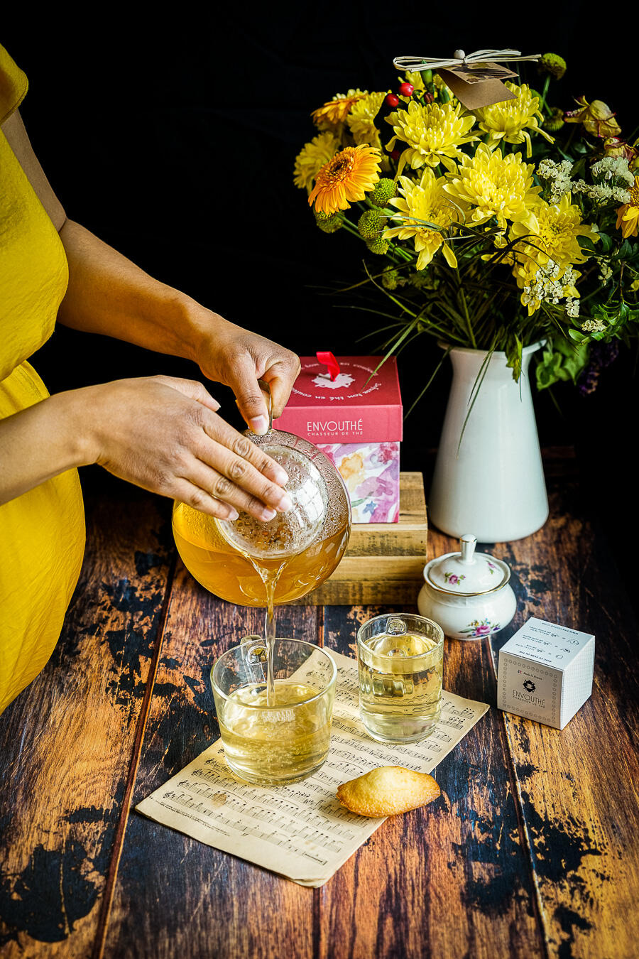 femme qui verse du thé dans un verre avec bouquet de fleurs jaunes