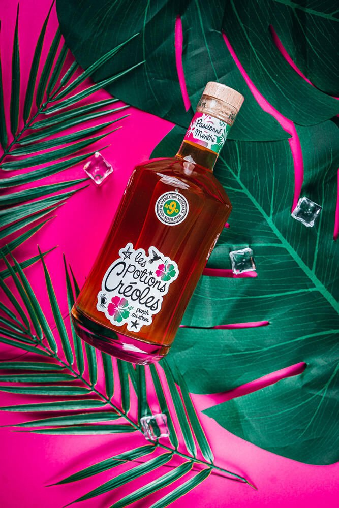 photographe culinaire de produit et ambiance bouteille les potions créoles sur fond rose et feuilles